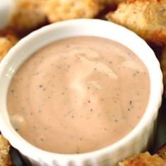 a white bowl filled with sauce sitting on top of fried food