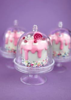 three small cakes with frosting and sprinkles under a glass dome