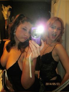 two beautiful young women taking a selfie in front of a mirror with a camera