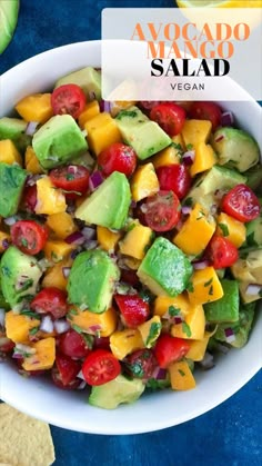 avocado mango salad in a white bowl on a blue table with tortilla chips