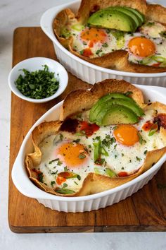 two white dishes filled with food on top of a wooden cutting board