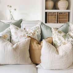 several pillows are stacked on top of each other in front of a book shelf with baskets