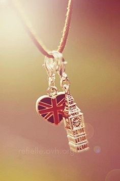 a silver necklace with a heart shaped charm hanging from it's end and the tower of london in the background