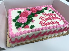 a birthday cake with pink frosting and roses on it in a white paper box