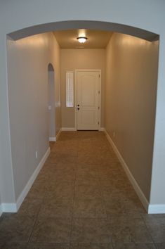 an empty room with tile flooring and white door in the center is lit by recessed lighting