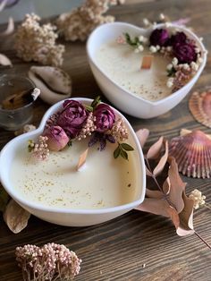 two heart shaped dishes with flowers in them sitting on a table next to seashells