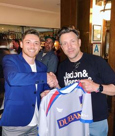 two men standing next to each other holding shirts