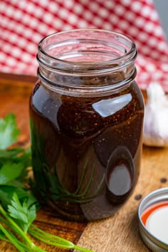 a jar filled with brown liquid next to some parsley on a wooden table top