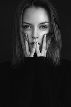 a black and white photo of a woman with her hands on her face looking at the camera