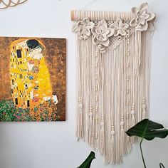 a wall hanging next to a painting on the wall and a plant in front of it