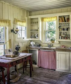 an old fashioned kitchen with wooden floors and white walls, has a red checkered tablecloth draped over the island