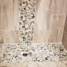 a walk in shower that has pebbles on the floor and tile around it, along with a toilet