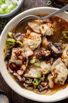 a white bowl filled with dumplings and sauce on top of a wooden table next to bowls