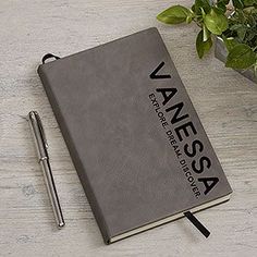 a notebook sitting on top of a wooden table next to a pen and potted plant