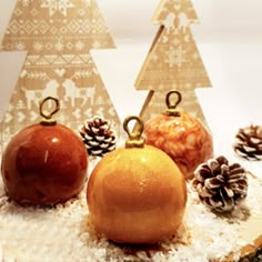 three oranges and two pine cones are sitting in the snow next to christmas trees