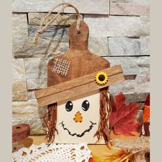 a wooden scarecrow with a sunflower on it's head sitting next to fall leaves