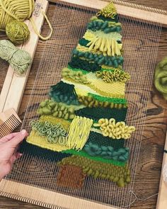 a person is weaving yarn on a loom with a wooden frame and green balls of yarn in the background