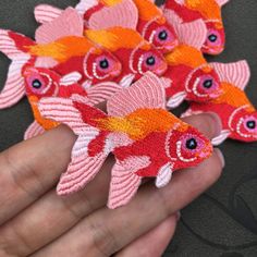 a hand is holding several red and orange fish brooches with eyes on them