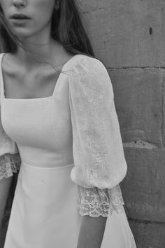 a woman in a white dress standing next to a brick wall with her hands on her hips