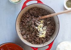 a pot filled with meat and sauce next to two bowls full of seasonings on a table