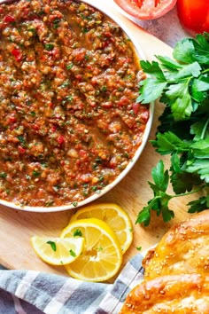 a close up of a bowl of food on a wooden table with bread and tomatoes