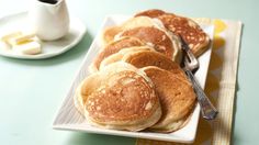 some pancakes are on a white plate with a fork and cup of coffee in the background