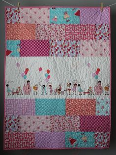 a pink and blue quilt hanging from a clothes line with balloons in the sky above it