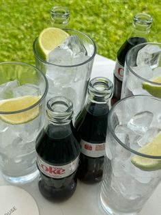 several bottles and glasses filled with ice and limes on top of a white table