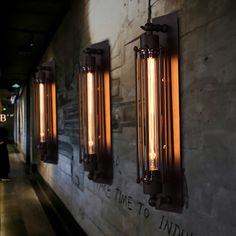 three light fixtures mounted to the side of a wall next to a person walking down a hallway