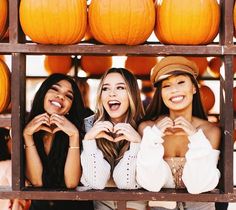 three beautiful young women standing next to each other in front of pumpkins on display