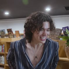 a man with curly hair is smiling and looking at his cell phone in the library