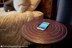 a cell phone sitting on top of a wooden table next to a bed with pillows