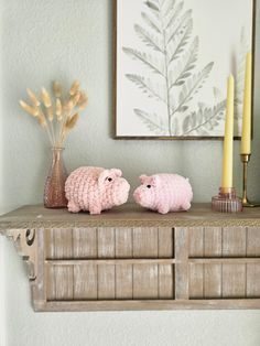 two pink crocheted sheep sitting on top of a wooden shelf next to candles