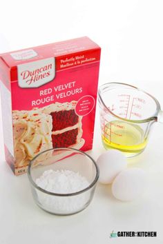 ingredients to make red velvet cake sitting on a white counter top, including eggs and flour