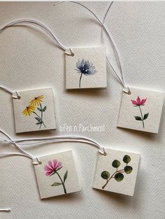 four small cards with flowers on them hanging from twine strings, one is white and the other is pink