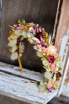 a wreath made out of dried flowers and feathers on a wooden bench in front of an old door