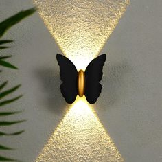 a butterfly shaped light on the wall next to a potted palm tree in front of it