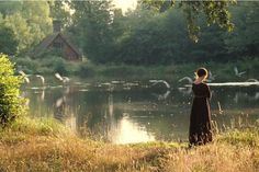 a woman standing in front of a body of water with birds flying above her head