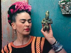 a woman holding up a small figurine in front of a blue wall