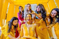 a group of women standing next to each other in front of a yellow wall with curtains