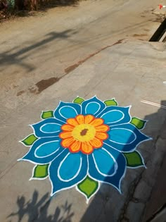 a blue and orange flower painted on the ground next to a street with trees in the background