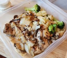 a plastic container filled with meat and veggies on top of a wooden table