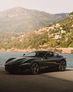 a black sports car parked on the side of a road next to a body of water