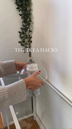 a woman is holding a water bottle in front of a glass shelf with plants on it