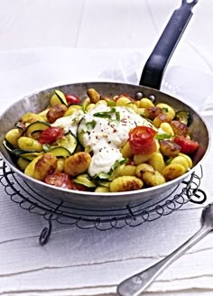 a pan filled with pasta and vegetables on top of a white table cloth next to a spoon