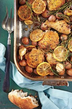 a pan filled with chicken, potatoes and lemons on top of a blue table cloth