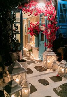 lanterns lit up in front of a house with red flowers on the windowsills