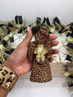 a hand holding a small teddy bear ornament in front of a leopard print background