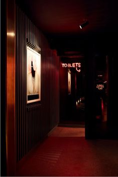 an empty hallway leading to a bathroom with red lights on the walls and a sign that reads toilets