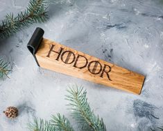 a bottle opener with the word hodor written on it next to pine branches and cones